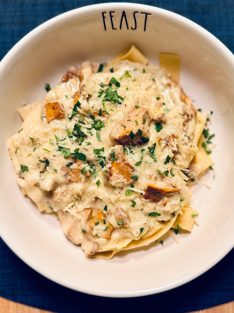 Cream-colored pasta bowl with "Feast" on the inner rim holds pappardelle with golden chanterelles in cream.